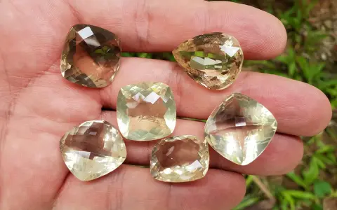 A hand holds six faceted lemon quartz gemstones, showcasing their pale yellow and brown hues. These stones are often associated with the lemon quartz meaning of clarity and optimism.