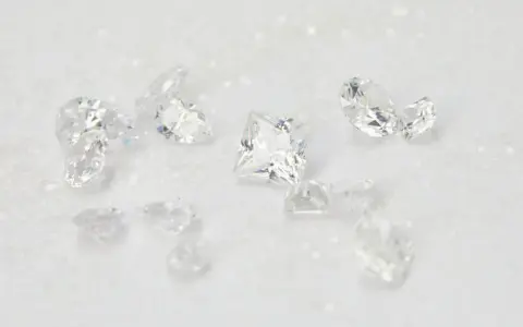 Scattered diamonds, some square-cut, others pear-shaped, on a white, glittery surface. These beautiful stones remind us of the dark reality of what is a blood diamond.