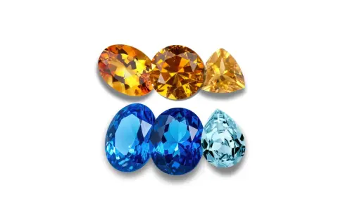 A collection of faceted gemstones, including warm orange and yellow topaz birthstones, and cool blue and aquamarine stones, arranged in two rows.