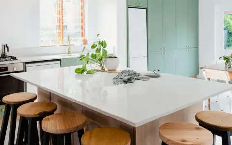 A modern kitchen island with a speckled synthetic quartz countertop, surrounded by wooden stools.