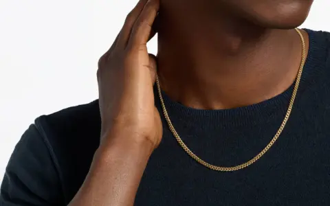 A man's hand touches his neck, showcasing a sleek gold chain length for men.