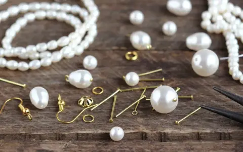 A collection of cultured pearls, meaning their natural beauty and value, are scattered with jewelry-making findings on a wooden surface, ready to be crafted into elegant pieces.