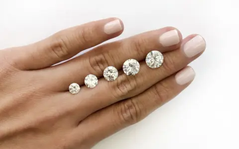 Five round brilliant cut diamonds are displayed on a hand, showing a progression in size. The largest diamond is what is considered a big diamond.
