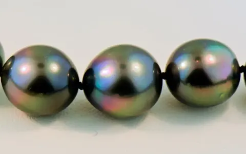 A close-up of a strand of dark, iridescent pearls with peacock green and purple overtones.