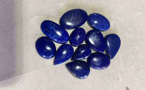 A collection of polished, deep blue Afghanistan gemstones, likely lapis lazuli, are scattered on a textured surface.