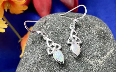 Silver Celtic knot earrings with opals, reminiscent of ancient Celtic birthstones, rest on a textured stone.