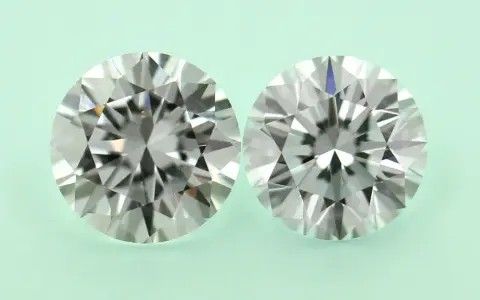 Two round brilliant cut diamonds, one a diamond simulant and the other lab grown, are shown side-by-side on a pale green background.