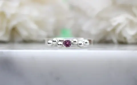 A silver ring with a central pink sapphire, the birthstone for September, surrounded by small silver spheres.