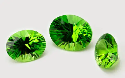 Three faceted peridots, the august 3rd birthstone, gleam with vibrant green light against a white background.