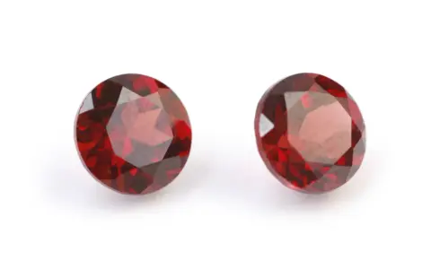 Two deep red, faceted gemstones, the traditional capricorn birthstone, are displayed on a white background.