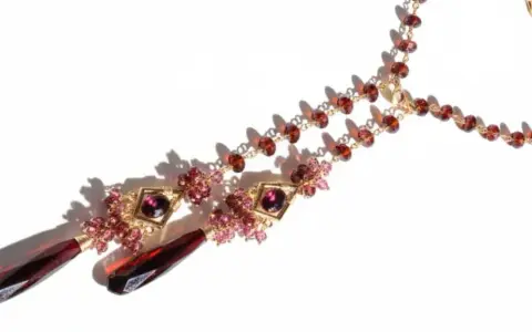 A gold necklace with various types of garnet, featuring deep red teardrop pendants and smaller faceted garnets in a rich, warm hue.
