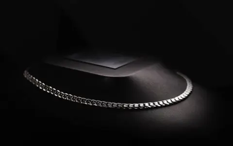 A sleek man platinum necklace rests on a dark, textured display.