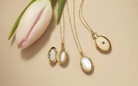 Gold lockets featuring mother of pearl, a lustrous material from shells, lie beside a delicate pink tulip.