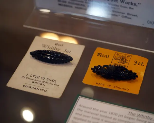 Two antique black jet stone brooches, one on a cream card from J. Lyth & Sons, Whitby, the other on a yellow card.