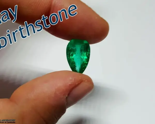 Fingers hold a pear-shaped emerald, the vibrant green gem representing the May birthstone.