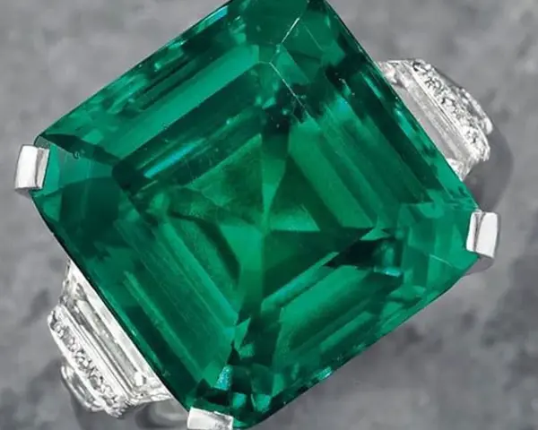 A stunning emerald ring, showcasing a large, square-cut green gemstone, possibly the most expensive gemstone, surrounded by smaller diamonds.