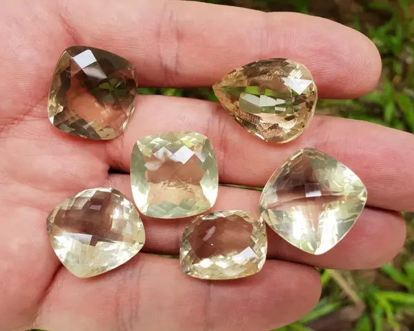 A hand holds six faceted lemon quartz gemstones, showcasing their pale yellow and brown hues. These stones are often associated with the lemon quartz meaning of clarity and optimism.