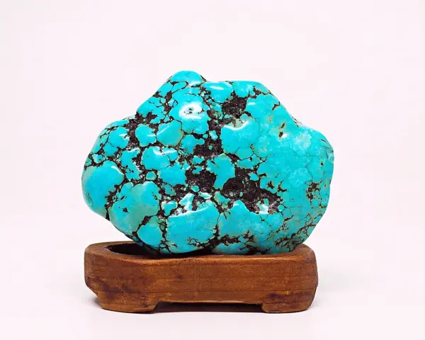 A vibrant turquoise stone, reminiscent of a Sagittarius stone, rests on a wooden stand. Its matrix pattern resembles a starry night sky.