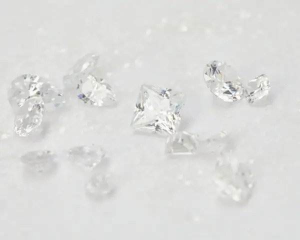Scattered diamonds, some square-cut, others pear-shaped, on a white, glittery surface. These beautiful stones remind us of the dark reality of what is a blood diamond.