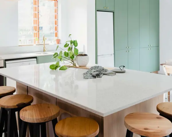 A modern kitchen island with a speckled synthetic quartz countertop, surrounded by wooden stools.