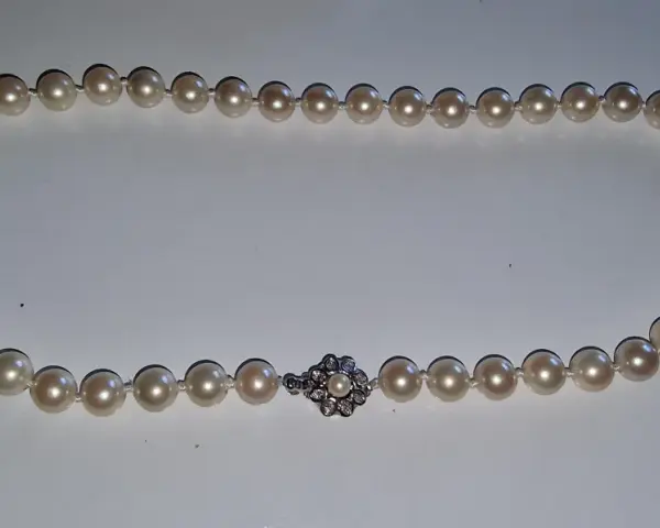 A pearl necklace with a diamond clasp. Learn how to tell if pearls are real by examining their luster and surface imperfections.