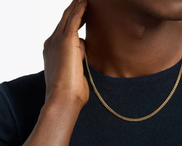 A man's hand touches his neck, showcasing a sleek gold chain length for men.