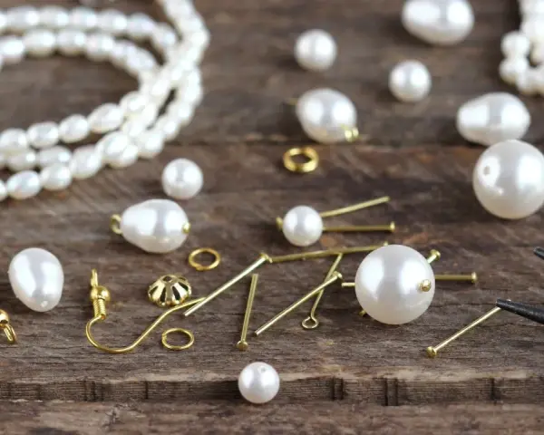 A collection of cultured pearls, meaning their natural beauty and value, are scattered with jewelry-making findings on a wooden surface, ready to be crafted into elegant pieces.