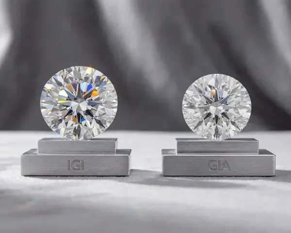 Two brilliant-cut diamonds, one labeled IGI and the other GIA, are displayed on pedestals. This highlights the difference between natural and simulated diamond grading.