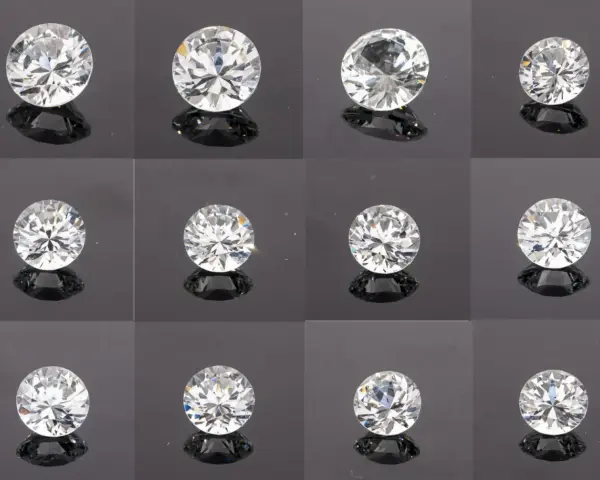Twelve sparkling stones that look like diamonds, each with brilliant facets, are arranged in a grid on a dark, reflective surface.