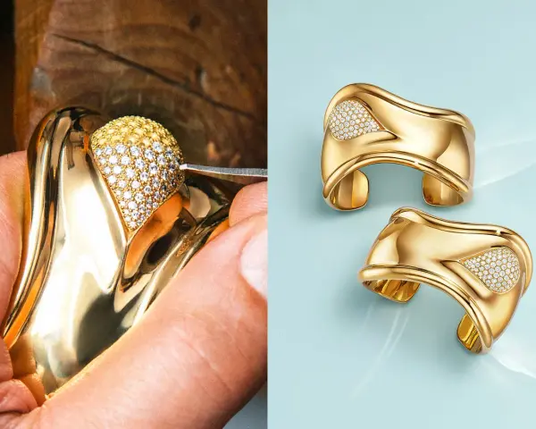 A jeweler meticulously sets diamonds on a gold ring, a testament to Elsa Peretti's exquisite designs. Two finished gold cuffs with diamond accents gleam on a light blue background.