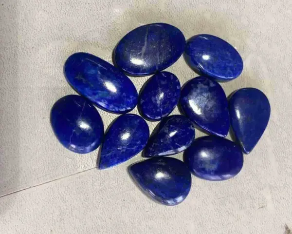 A collection of polished, deep blue Afghanistan gemstones, likely lapis lazuli, are scattered on a textured surface.