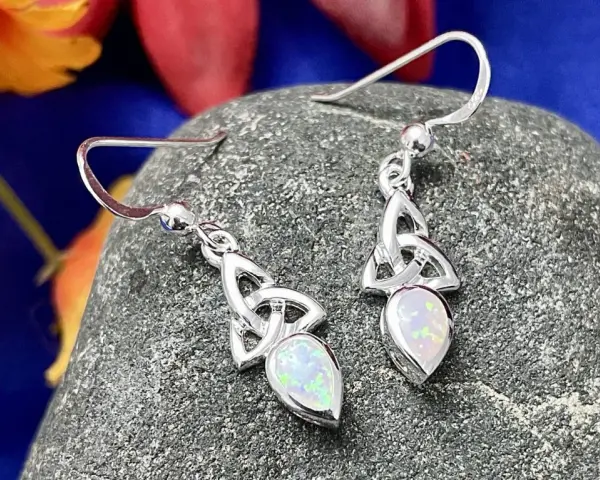 Silver Celtic knot earrings with opals, reminiscent of ancient Celtic birthstones, rest on a textured stone.