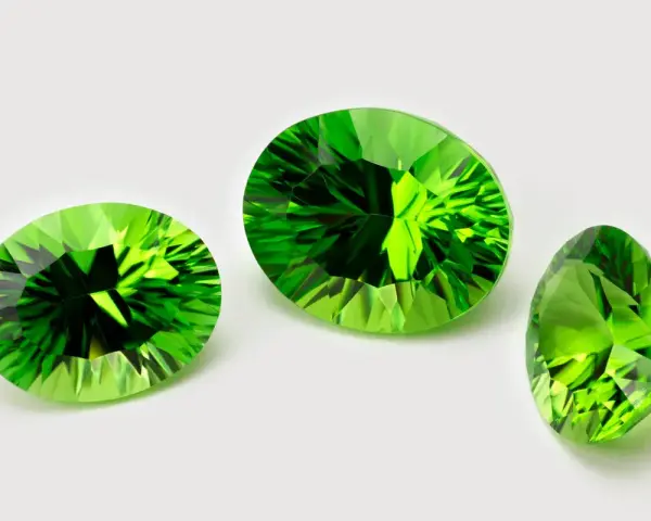 Three faceted peridots, the august 3rd birthstone, gleam with vibrant green light against a white background.
