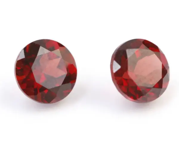 Two deep red, faceted gemstones, the traditional capricorn birthstone, are displayed on a white background.