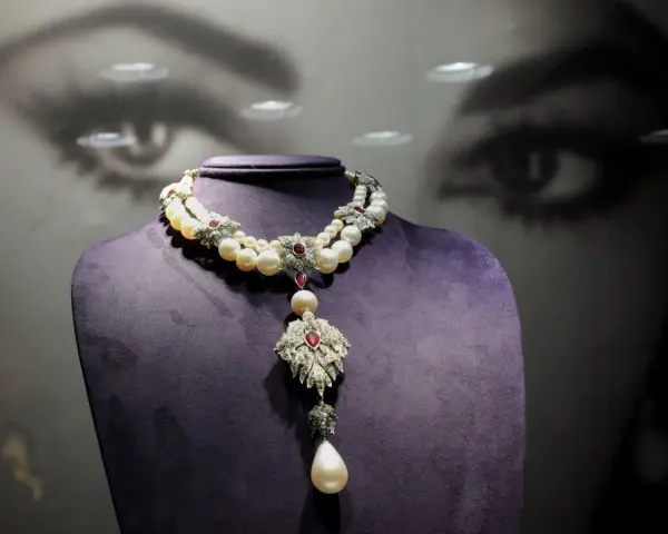 A stunning pearl and ruby necklace, reminiscent of "La Peregrina," drapes elegantly over a purple bust.