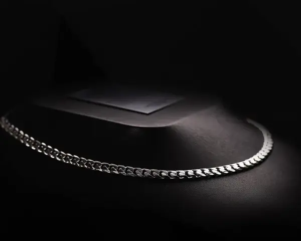 A sleek man platinum necklace rests on a dark, textured display.