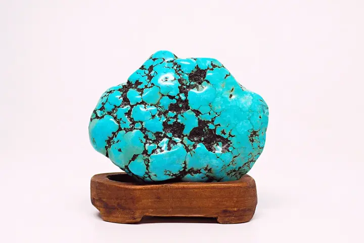 A vibrant turquoise stone, reminiscent of a Sagittarius stone, rests on a wooden stand. Its matrix pattern resembles a starry night sky.
