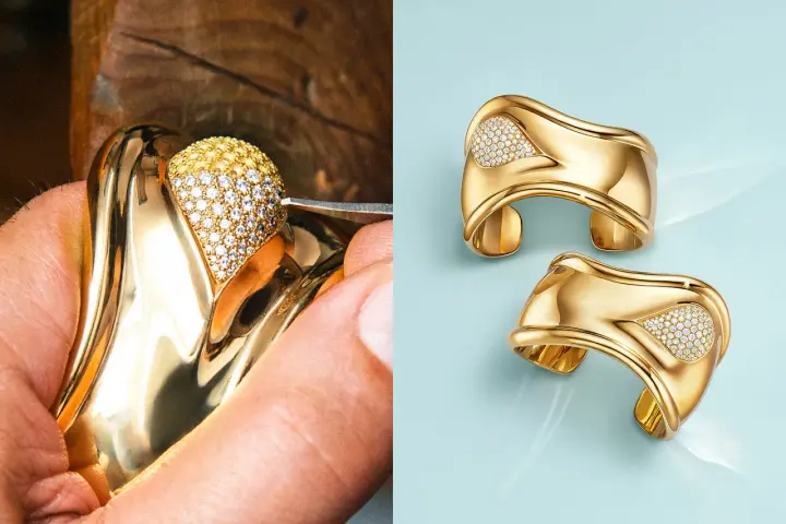 A jeweler meticulously sets diamonds on a gold ring, a testament to Elsa Peretti's exquisite designs. Two finished gold cuffs with diamond accents gleam on a light blue background.