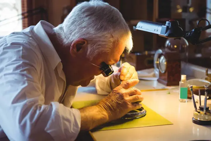 A watchmaker, wearing a loupe, meticulously works on a watch, demonstrating how to fix a watch with precision tools.