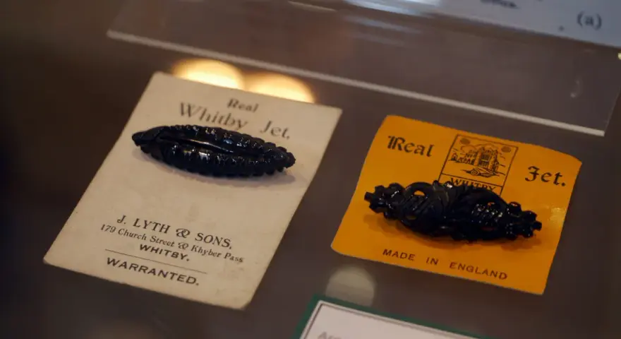 Two antique black jet stone brooches, one on a cream card from J. Lyth & Sons, Whitby, the other on a yellow card.