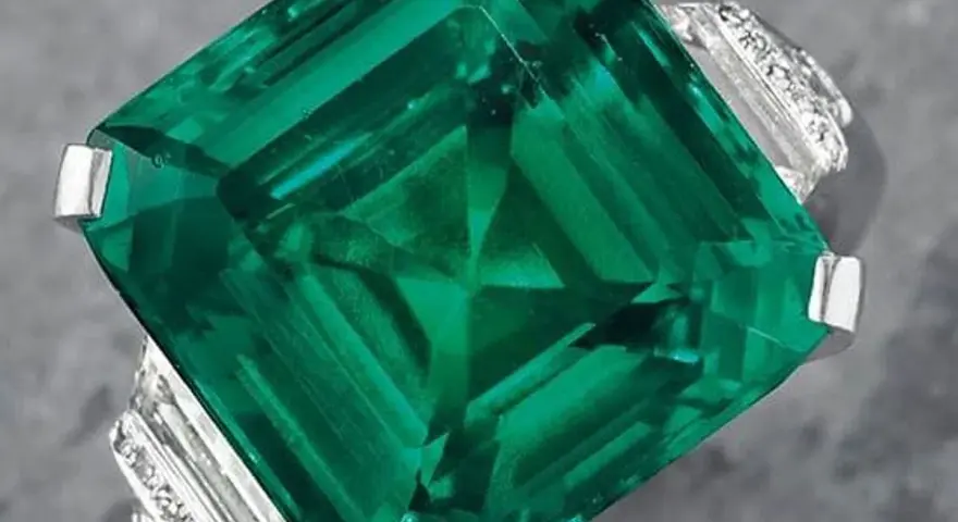 A stunning emerald ring, showcasing a large, square-cut green gemstone, possibly the most expensive gemstone, surrounded by smaller diamonds.