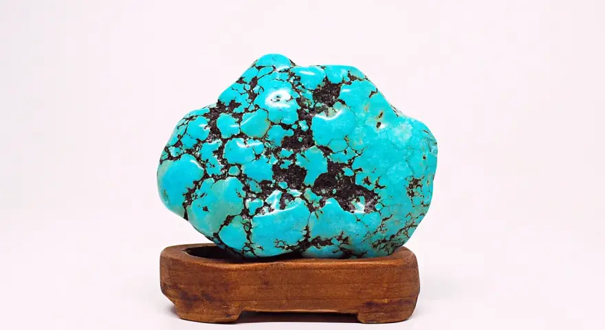 A vibrant turquoise stone, reminiscent of a Sagittarius stone, rests on a wooden stand. Its matrix pattern resembles a starry night sky.