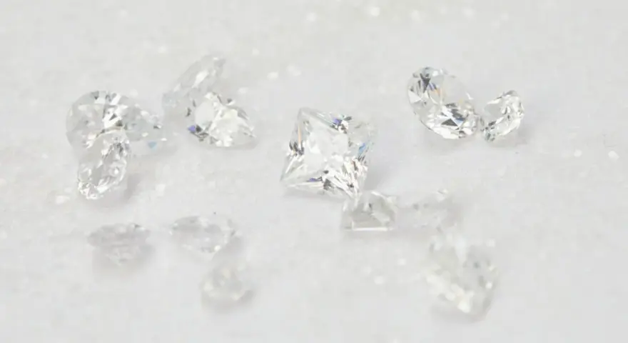 Scattered diamonds, some square-cut, others pear-shaped, on a white, glittery surface. These beautiful stones remind us of the dark reality of what is a blood diamond.