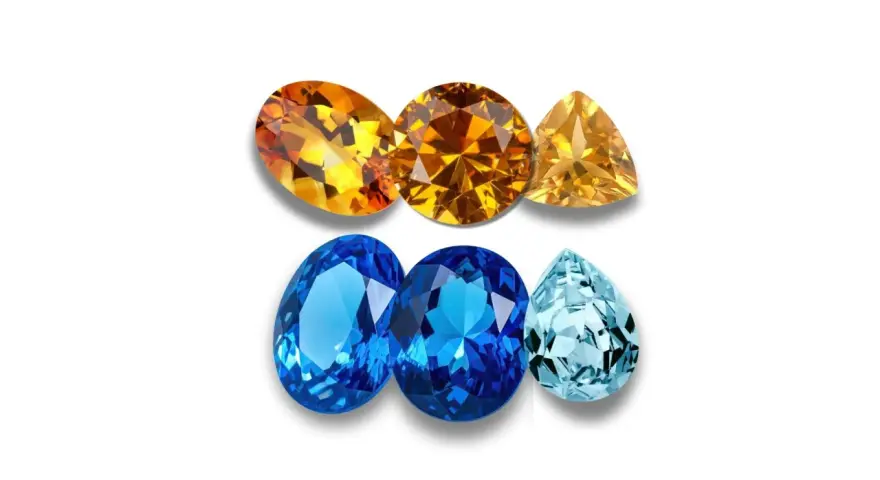 A collection of faceted gemstones, including warm orange and yellow topaz birthstones, and cool blue and aquamarine stones, arranged in two rows.