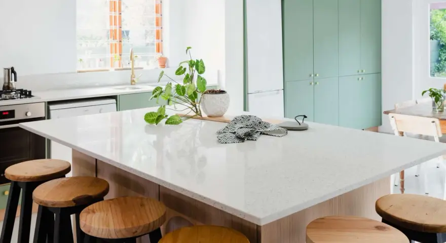 A modern kitchen island with a speckled synthetic quartz countertop, surrounded by wooden stools.