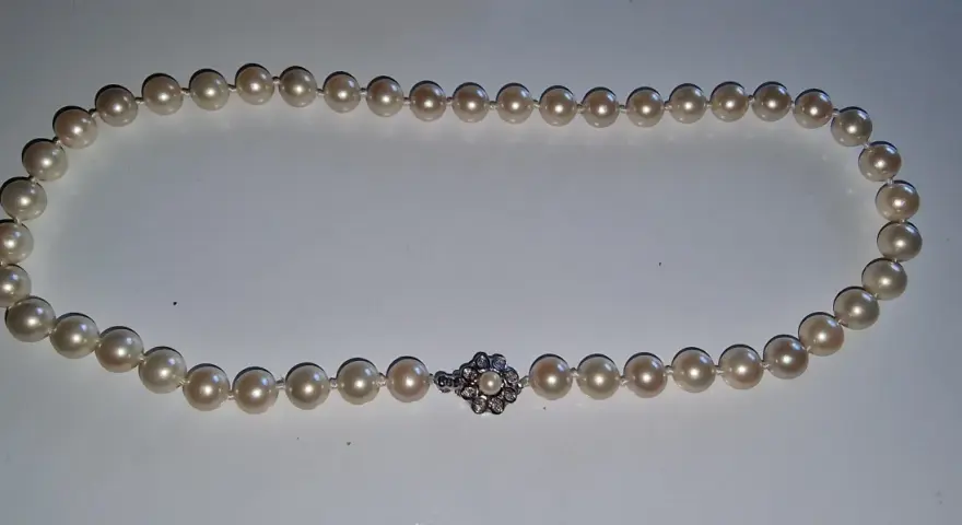 A pearl necklace with a diamond clasp. Learn how to tell if pearls are real by examining their luster and surface imperfections.