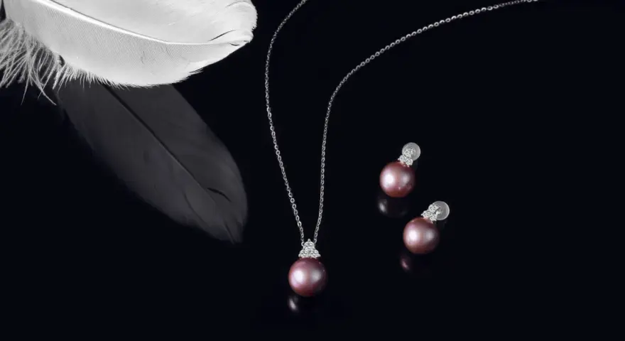 A delicate necklace and earrings featuring pink pearls, symbolizing love and purity. A white feather rests nearby, adding an ethereal touch.