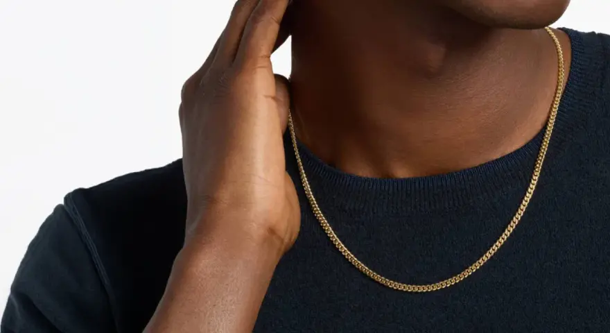 A man's hand touches his neck, showcasing a sleek gold chain length for men.