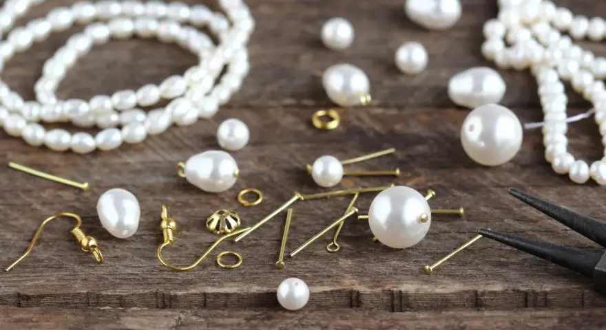 A collection of cultured pearls, meaning their natural beauty and value, are scattered with jewelry-making findings on a wooden surface, ready to be crafted into elegant pieces.