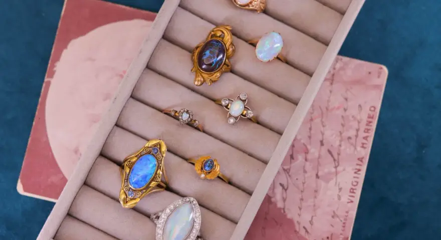A collection of antique jewelry with opal stones, featuring rings with iridescent opals in gold settings, displayed in a velvet ring holder.